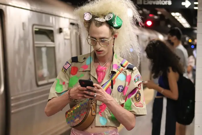 someone in a modified, colorful Boy Scout shirt stands on a subway platform